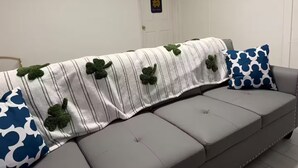 Ein Wohnzimmer mit grauem Sofa, einer gestreiften Decke mit Kleeblatt-Muster und einem blauen Kissen.