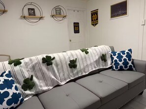 Ein Wohnzimmer mit grauem Sofa, einer gestreiften Decke mit Kleeblatt-Muster und einem blauen Kissen.