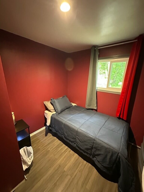 A bedroom with a bed, a nightstand, a window with curtains, and a view of greenery outside.