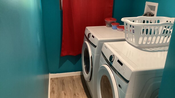 A laundry room with two washing machines, a red towel, and a white laundry basket. - 2 bedroom home in Fort Frances Ontario (Fort Frances)