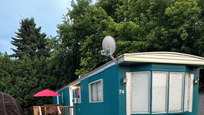 A single-story mobile home with a number '74' on the side, a satellite dish, and a small porch with a red umbrella. - 2 bedroom home in Fort Frances Ontario (Fort Frances)