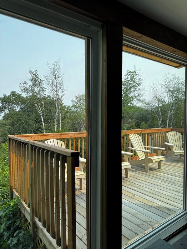 A wooden deck with Adirondack chairs and a glass door leading to a view of trees.