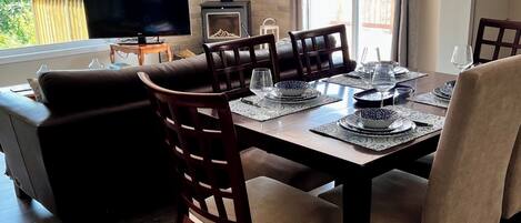 A dining area with a wooden table, chairs, and a television on a stand.