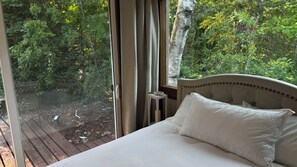 A bedroom with a bed, curtains, and a view of a forest through a window.