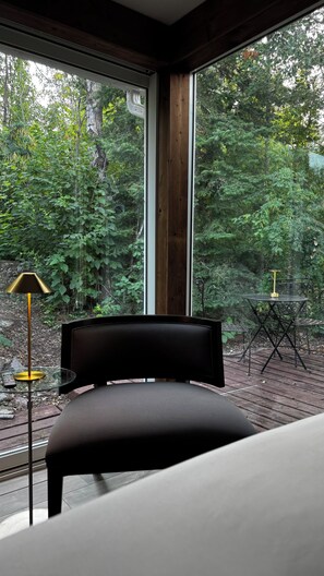 Ein modernes Schlafzimmer mit großem Fenster, einem Bett, einem kleinen Tisch mit Lampe und einem Sessel.