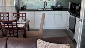 Une cuisine moderne avec des meubles blancs, un réfrigérateur en acier inoxydable et un coin repas agrémenté d’un canapé en cuir marron et d’un coussin décoratif.