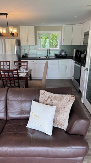 A modern kitchen with white cabinets, a stainless steel refrigerator, and a dining area with a brown leather couch and a decorative pillow.
