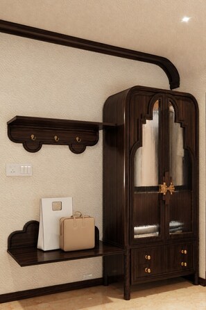 Un mueble de madera oscura con puerta de cristal, una pared color beige y un estante con un objeto blanco y una bolsa color beige.
