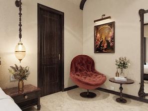 A room with a dark wooden door, a red velvet chair, a small table with a vase, and a wall-mounted picture.