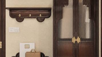 Una habitación con cama, un armario de madera oscura con espejo, un estante sobre la cama y una mesita con un bolso y un objeto blanco.