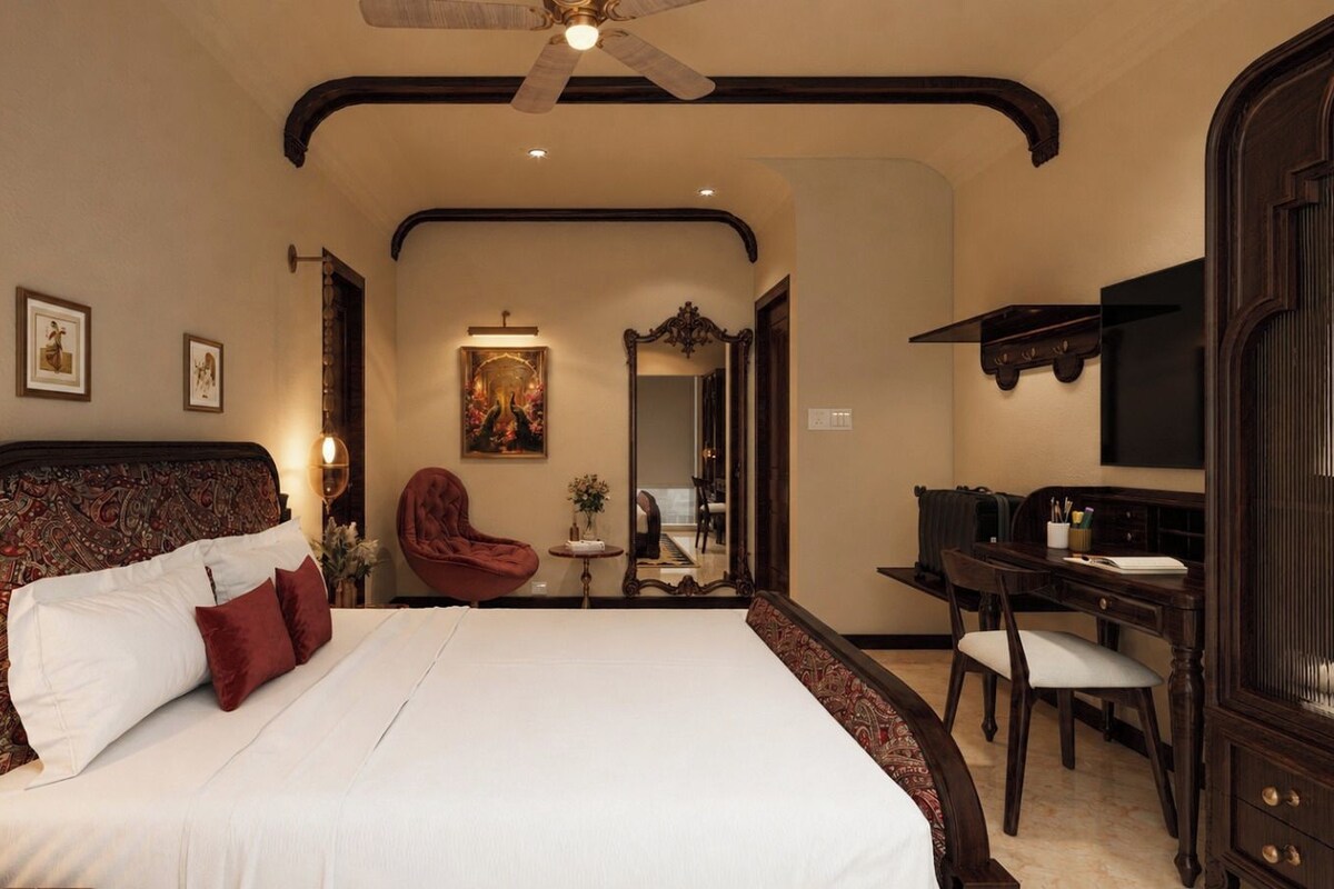 A hotel room with a large bed, a desk, a chair, a ceiling fan, and a mirror.