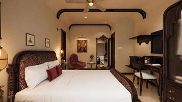 A hotel room with a large bed, a desk, a chair, a ceiling fan, and a mirror.