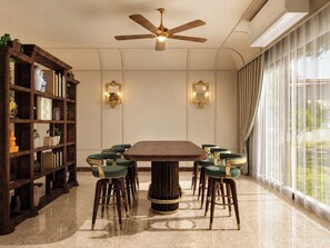 A dining area with a round table surrounded by chairs, a ceiling fan, and a bookshelf with various items.