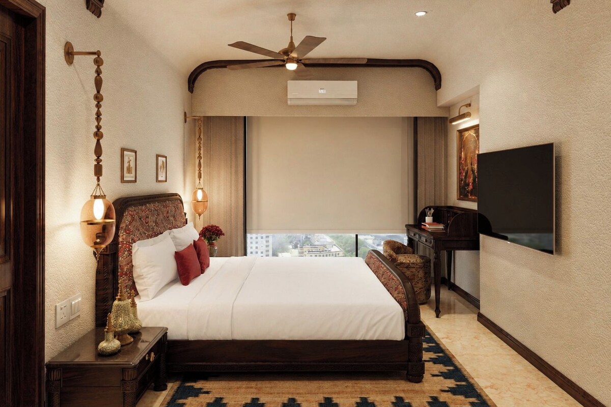 A hotel room with a large bed, a ceiling fan, a flat-screen TV, and a view of the city.