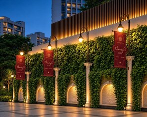 Fachada de edifício com jardins verticais, janelas em arco e banners iluminados.