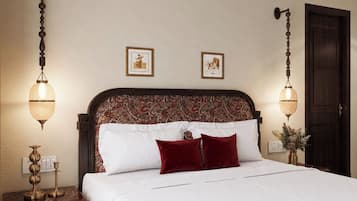 Een slaapkamer met een groot bed, twee wandlampen, een houten hoofdbord met een paisley dessin, en een donkere houten deur.