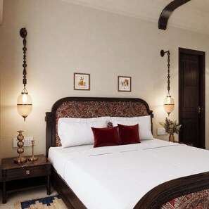 A bedroom with a large bed, two wall-mounted lamps, a wooden headboard with a paisley pattern, and a dark wooden door.