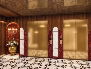 A hotel lobby with a marble floor, a large vase with flowers, and two elevators with marble panels.