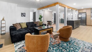 Una sala moderna con un sofá negro, sillones naranja y una mesita de centro.