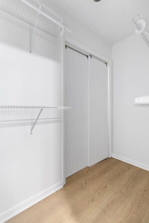 Ein Zimmer mit Holzboden, weißen Wänden und einer weißen Decke. Es gibt einen weißen Deckenventilator, eine weiße Heizkörper und ein weißes Regal.