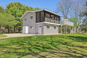 Een modern huis met twee verdiepingen en een groot balkon, omgeven door een verzorgd gazon en bomen.