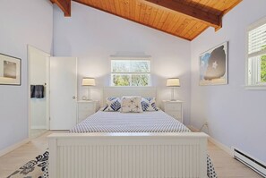 Ein Schlafzimmer mit einem Bett, zwei Nachttischen mit Lampen, einem Fenster und einer Tür.