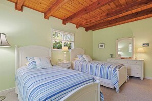 Een slaapkamer met twee bedden, een raam, een nachtkastje, een dressoir en een houten plafond.