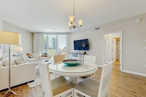 A modern living room with a dining area, a flat-screen TV mounted on the wall, and a view of the outside. - 2407 New Listing Special ~ Book Sept 7th ~ Pools ~ Gym ~ Onsite Restaurant & Bar (Destin)