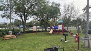 Um parque com parquinho, banco e lixeira.