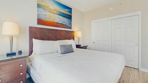 Quarto de hotel com uma cama grande, duas luminárias de cabeceira, um quadro acima da cama e uma porta branca.
