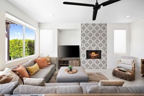 Ein modernes Wohnzimmer mit großem Fenster, Flachbildfernseher, Kamin und Deckenventilator.
