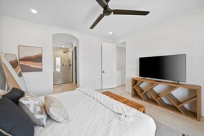 Ein Schlafzimmer mit einem Bett, einem Fernseher auf einem Holzboden, einem Deckenventilator und einer Duschkabine.