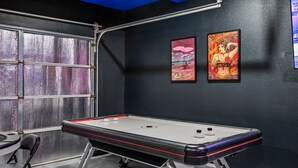 Una habitación con mesa de juego de discos, dos cuadros enmarcados y ventana con vistas.