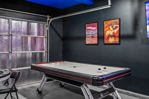A room with a shuffleboard table, two framed artworks, and a window with a view. - Heron by Nest Villas | Entertainers Dream Backyard (Indio)