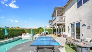 Una piscina con mesa de ping pong, sillas de descanso y zona de barbacoa.