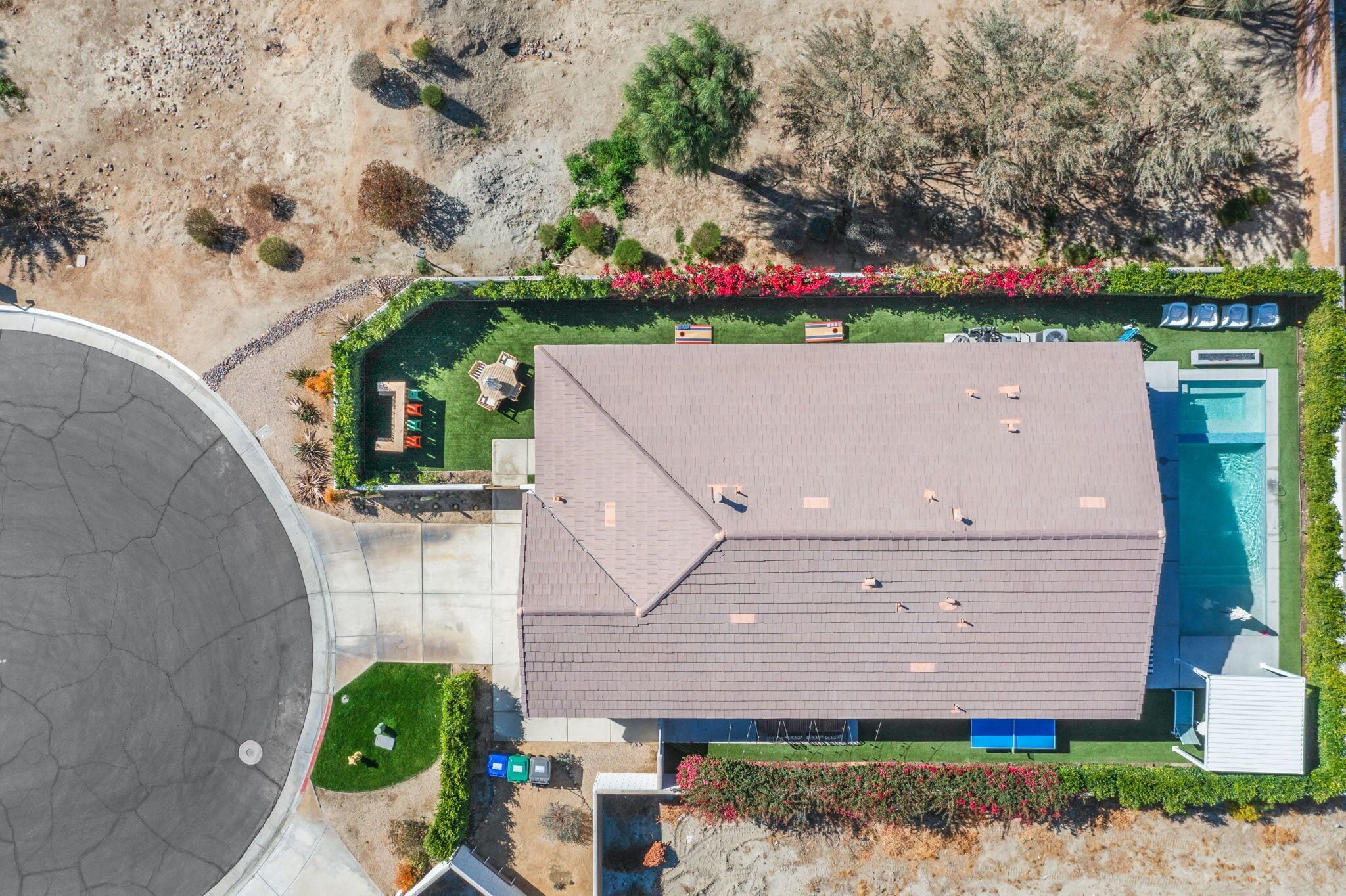 An aerial view of a residential property with a swimming pool, a covered patio, and a landscaped garden.