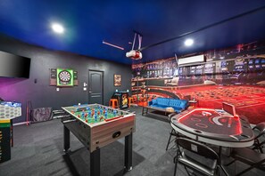 A room with a foosball table, dartboard, and a slot machine. - Phoebe by Nest Villas | Private Escape w Game Room (Indio)