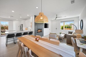 A modern kitchen with a central island, a dining area with a long table, and a living space with a sofa and a TV. - Phoebe by Nest Villas | Private Escape w Game Room (Indio)