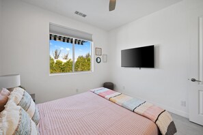 A bedroom with a bed, a window, a wall-mounted TV, and a door. - Phoebe by Nest Villas | Private Escape w Game Room (Indio)