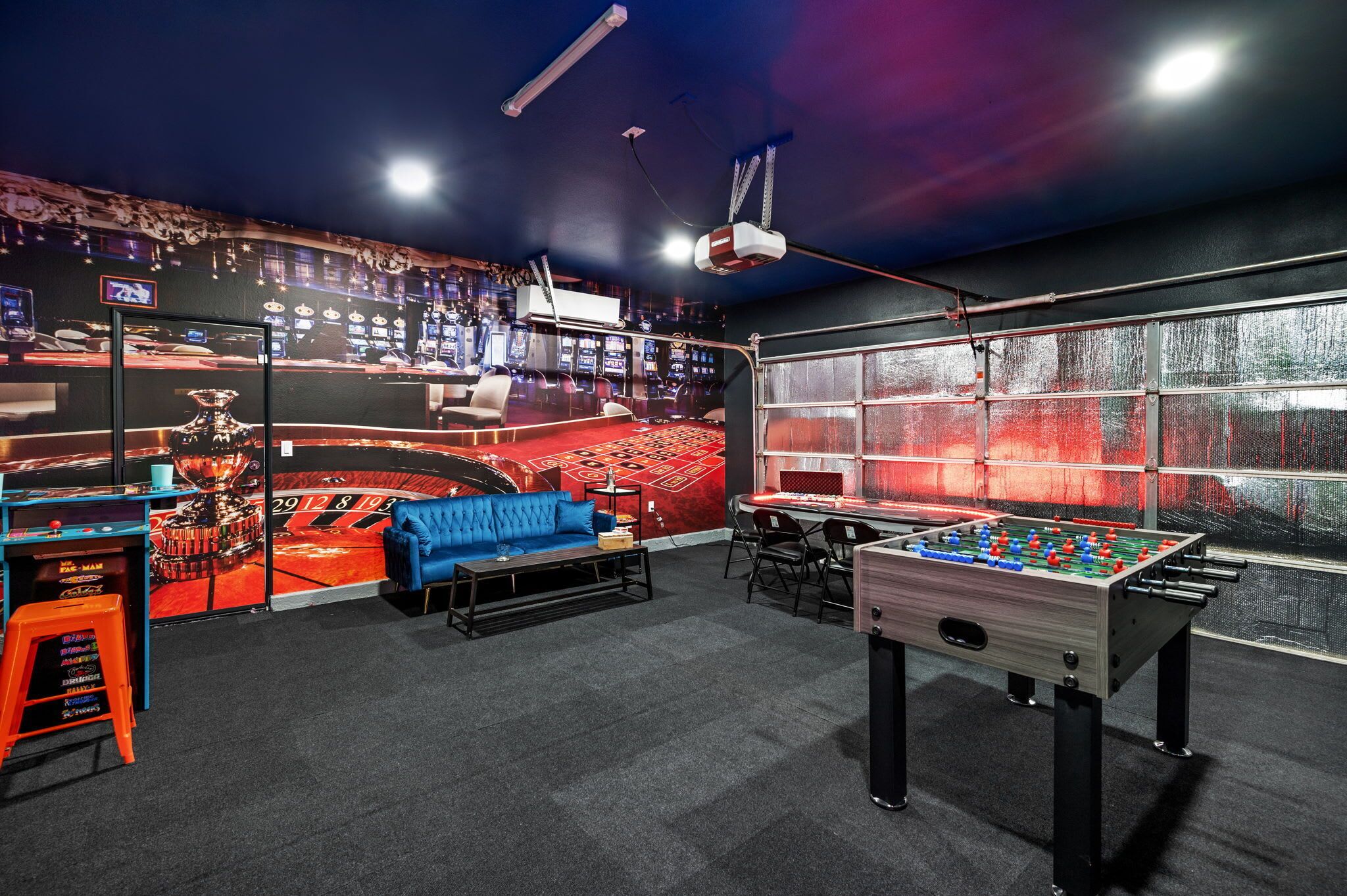 A room with a foosball table, a blue sofa, and a slot machine.