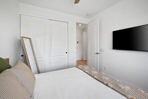 Makuuhuone, jossa on sänky, seinälle asennettu televisio ja ovi, joka johtaa toiseen huoneeseen.