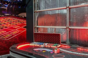 Ein Craps-Tisch mit Spielchips und Karten, ein Fenster mit Insektenschutzgitter und ein rot ausgelegter Teppichboden.