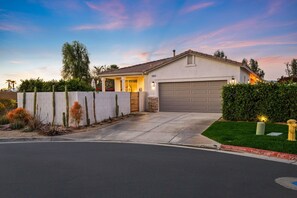 A residential house with a garage, a driveway, and a well-maintained garden with cacti and shrubs. - Phoebe by Nest Villas | Private Escape w Game Room (Indio)