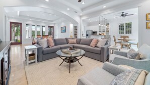 Ein geräumiges Wohnzimmer mit einem grauen Ecksofa, einem Couchtisch und einem Deckenventilator.