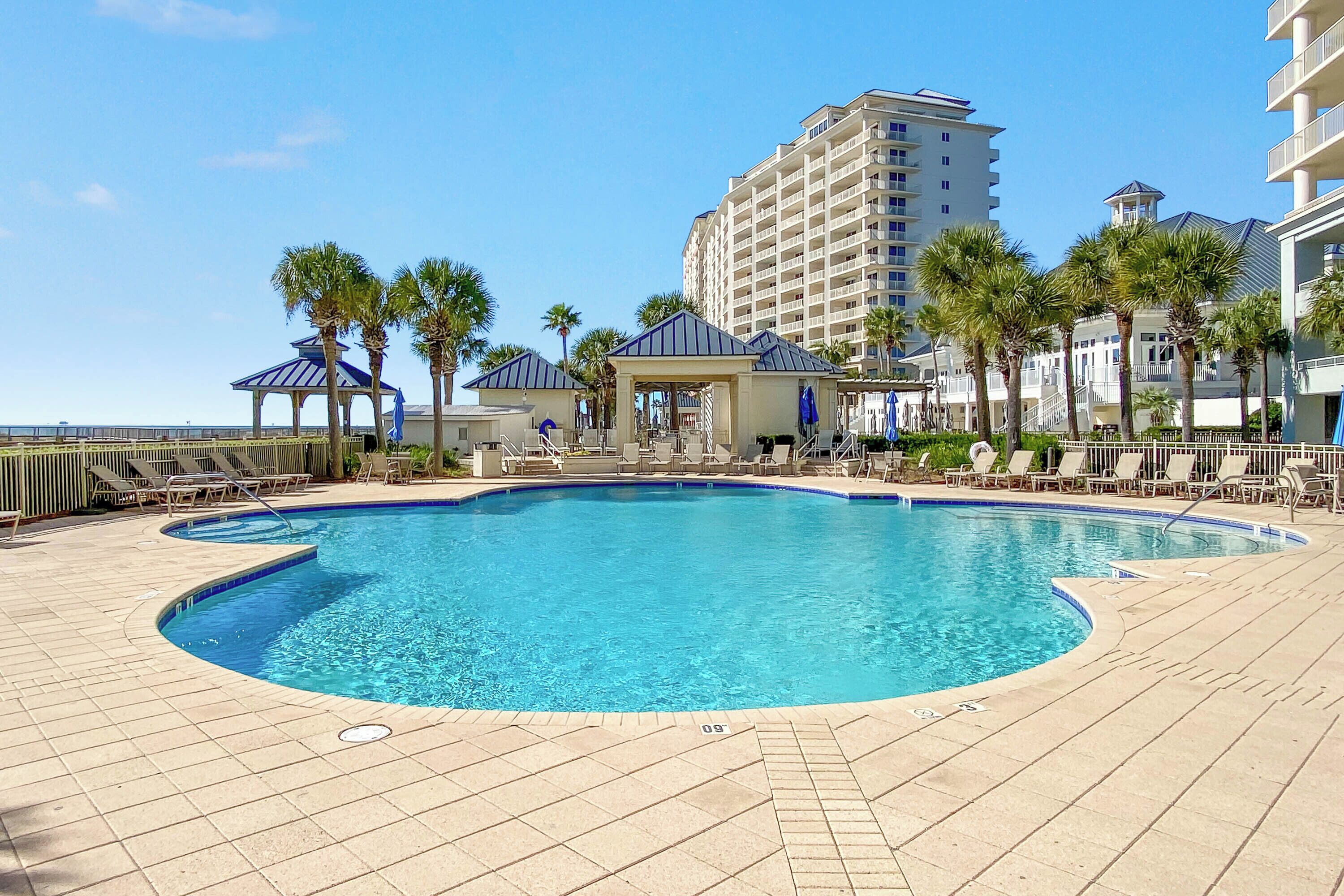 A swimming pool with lounge chairs and palm trees, surrounded by a high-rise building.