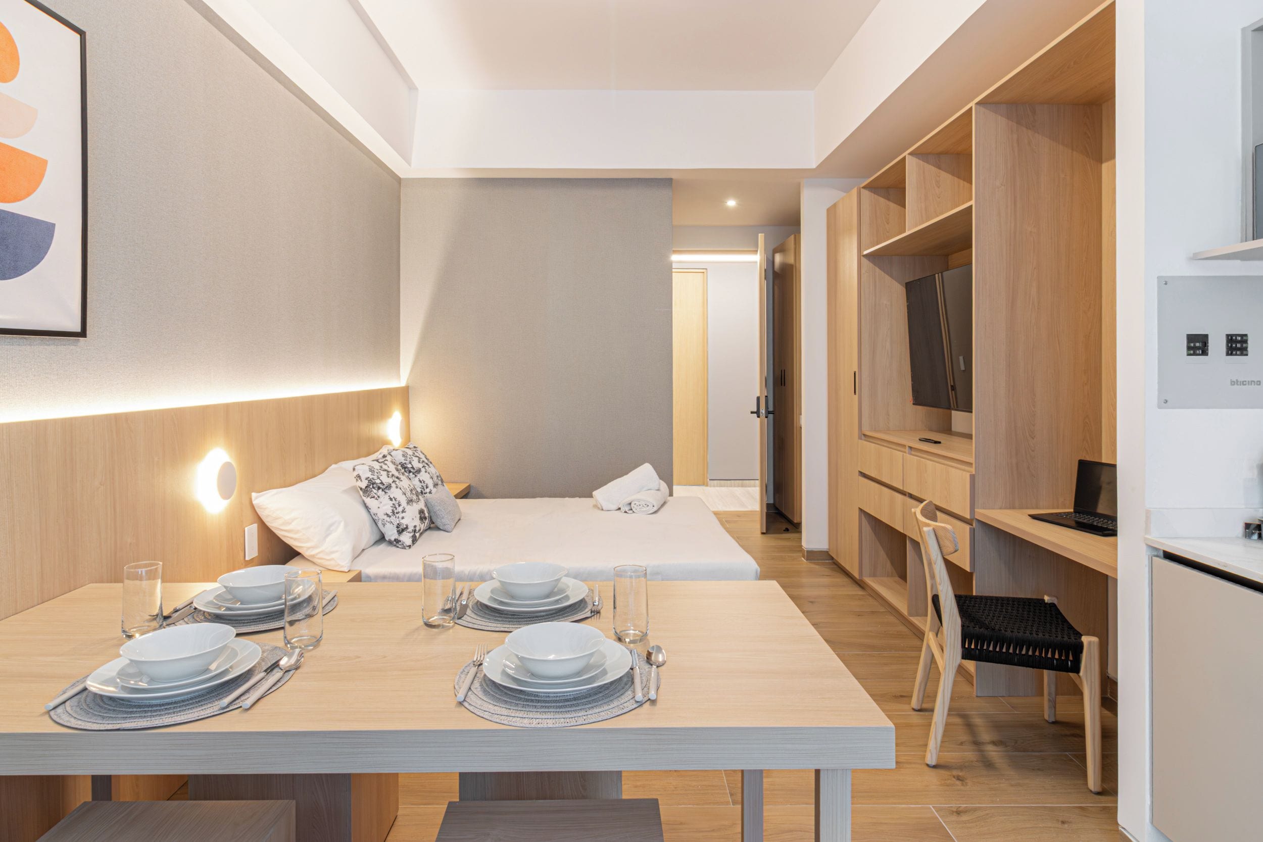 A modern hotel room with a dining area, a bed, and a kitchenette.