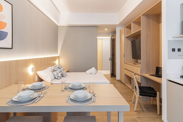 Una habitación de hotel moderna con zona de comedor, cama y kitchenette.