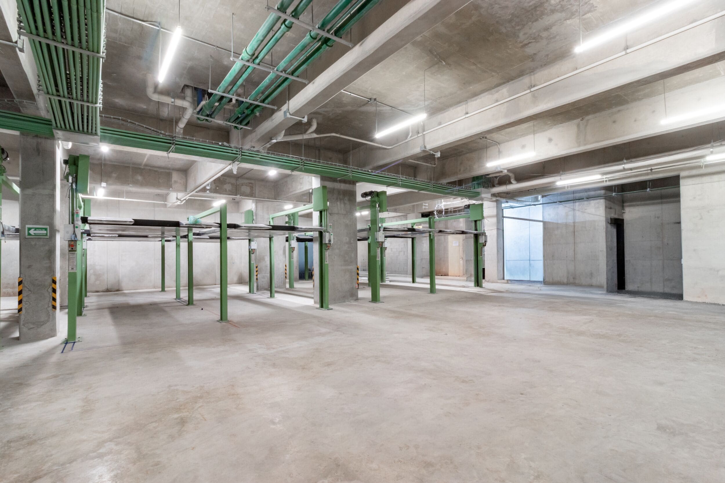 An indoor parking garage with concrete pillars, overhead pipes, and a clean, empty floor.