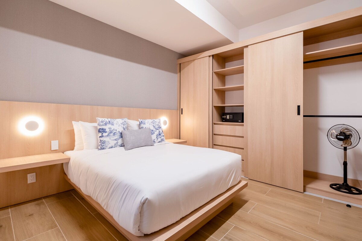 A modern bedroom with a bed, bedside tables, a wardrobe, and a standing fan.