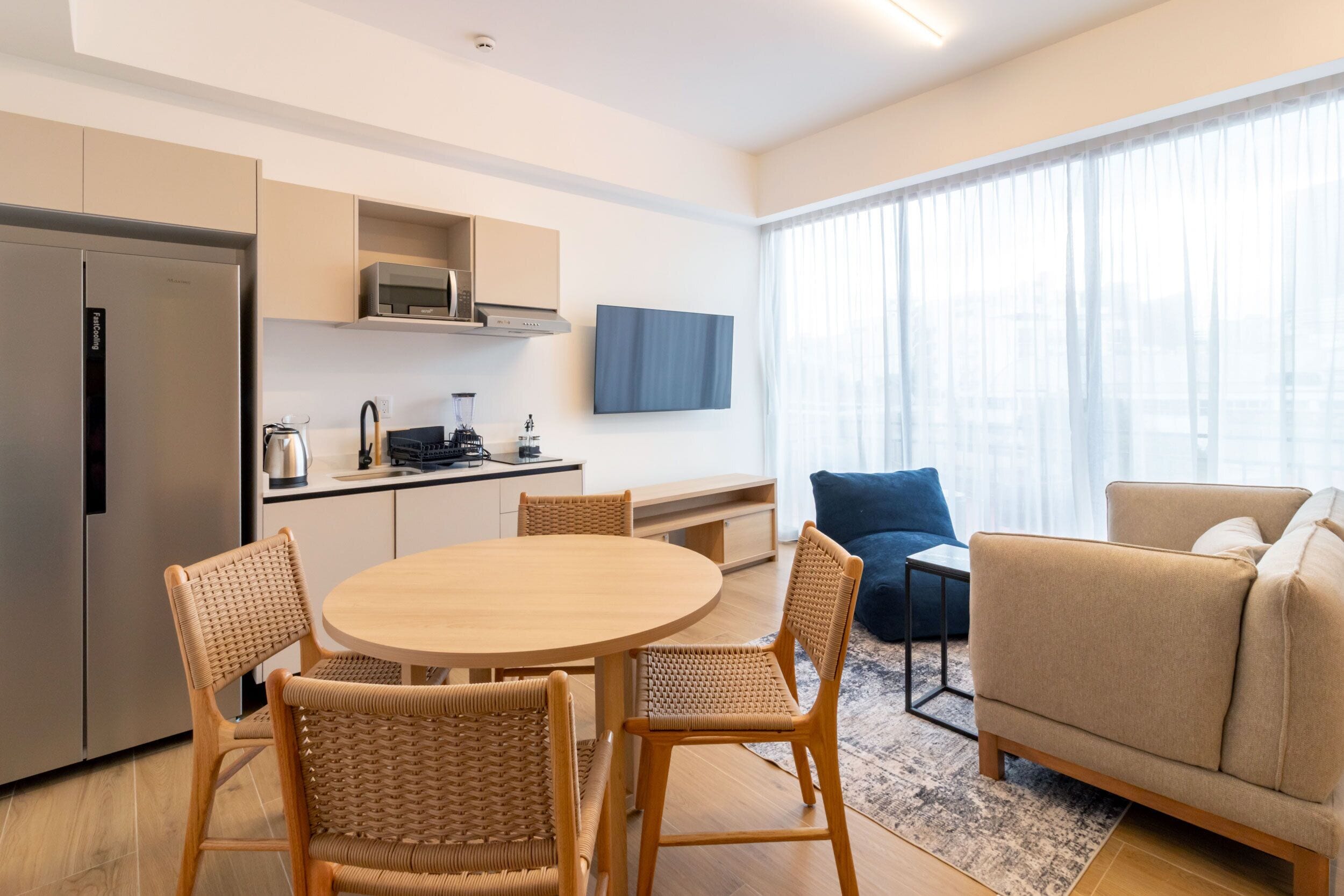 A modern living room with a round wooden table, wicker chairs, a beige sofa, and a blue armchair.